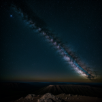The Milky Way galaxy gracefully arches over a crater rim, creating a breathtaking night sky view ideal for stargazers and photographers.