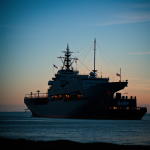 A ship silhouette elegantly set against a backdrop of a vast, star-filled blue sky, capturing the tranquility and mystery of nighttime maritime travel.