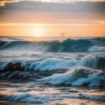 A captivating sunset with vibrant colors over ocean waves crashing on rocky shore, showcasing nature's beauty and tranquility.