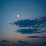 An enchanting view of the moon rising behind scattered clouds, casting a mystical glow across the night sky.