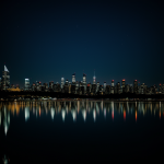 A stunning view of a night city skyline reflecting on still water, showcasing the vibrant city lights against the dark sky.