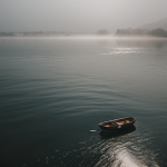 A small boat drifts on calm waters surrounded by a gentle morning mist, creating a serene and tranquil atmosphere perfect for reflection.