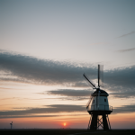 A picturesque windmill silhouetted against a vibrant sunrise, showcasing the harmonious blend of human craftsmanship and natural beauty.