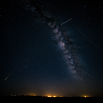 A meteor streaks across a starry night sky, illuminating the horizon with its brilliant trail, showcasing the beauty of celestial phenomena.