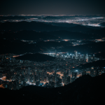 A stunning view of a vibrant night cityscape from a mountain top, showcasing the mesmerizing city lights against a serene night sky.