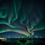 A breathtaking view of the Northern Lights casting vibrant colors over the serene Iceberg Bay, with massive icebergs silhouetted against the night sky.