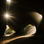 Sunlight streams through a cave's entrance, illuminating the stone walls with a warm glow, showcasing nature's beauty and wonder.